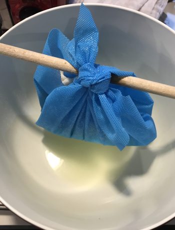 ricotta cheese hung in cheesecloth over a bowl to strain
